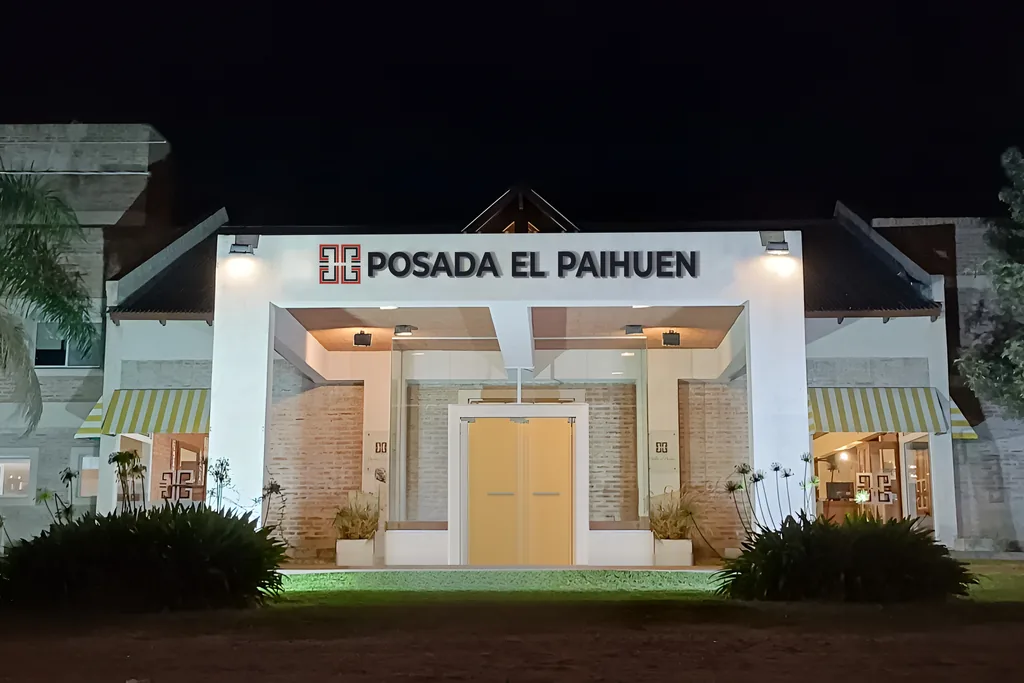 Frente de Posada El Paihuen de noche, con el cartel iluminado sobre la entrada